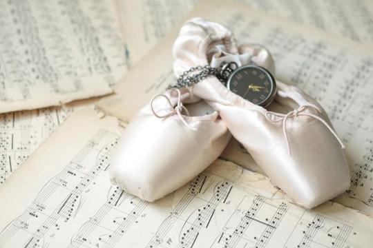 Ballet shoes and old watch laying on the old piano musical notes